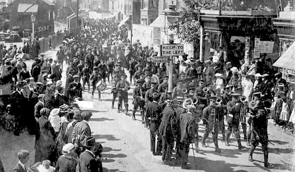 A regiment of soliders led by buglers marching along a street, off to train for war